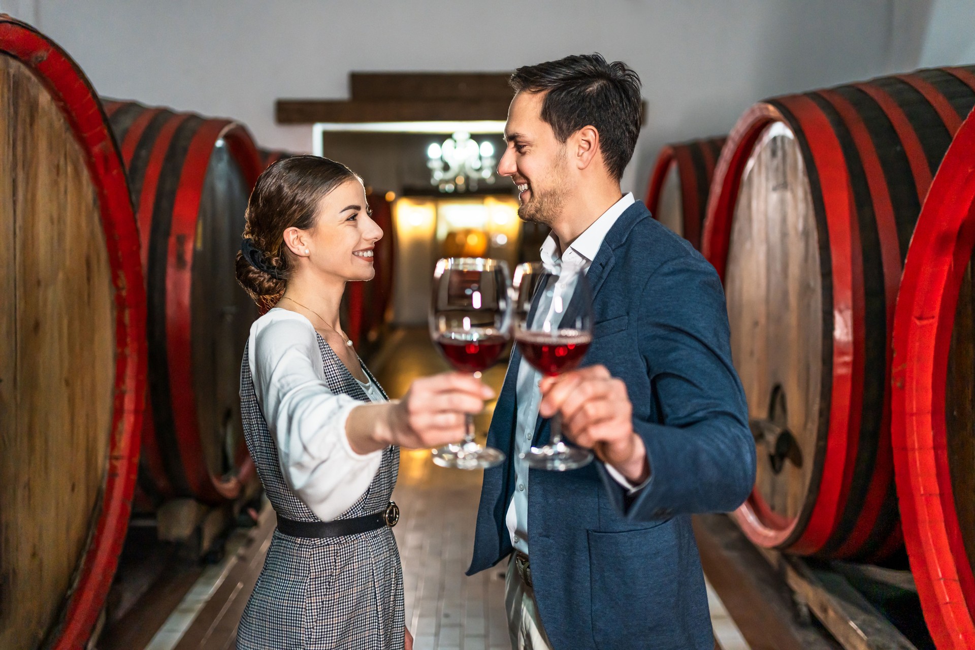 Young man and woman toasting with red wine in cellar with wooden barrels