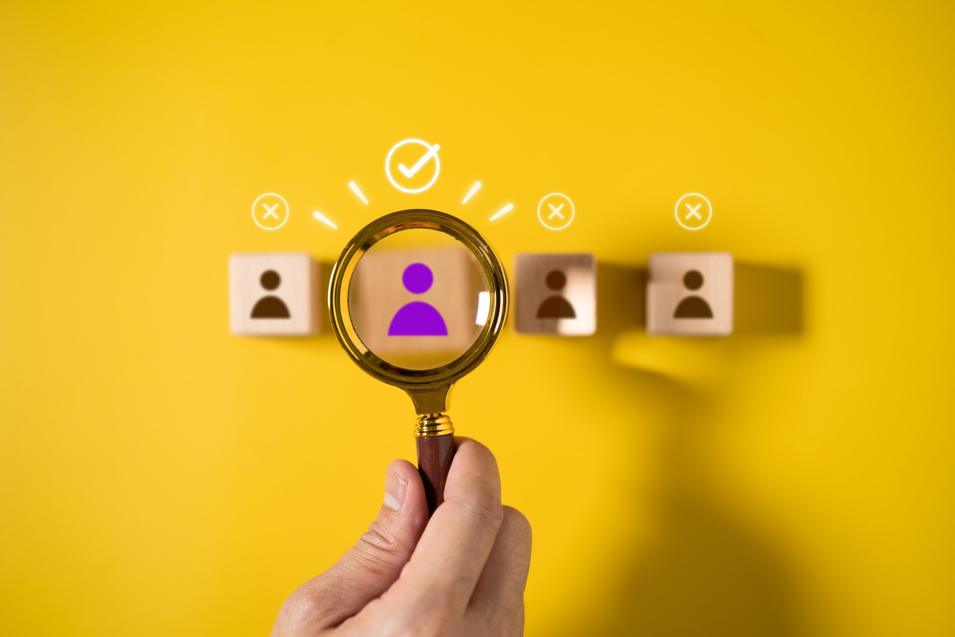 Male hand holding magnifying glass searching for wooden dice icon with people icon on yellow background, leadership recruitment concept or recruitment in organization