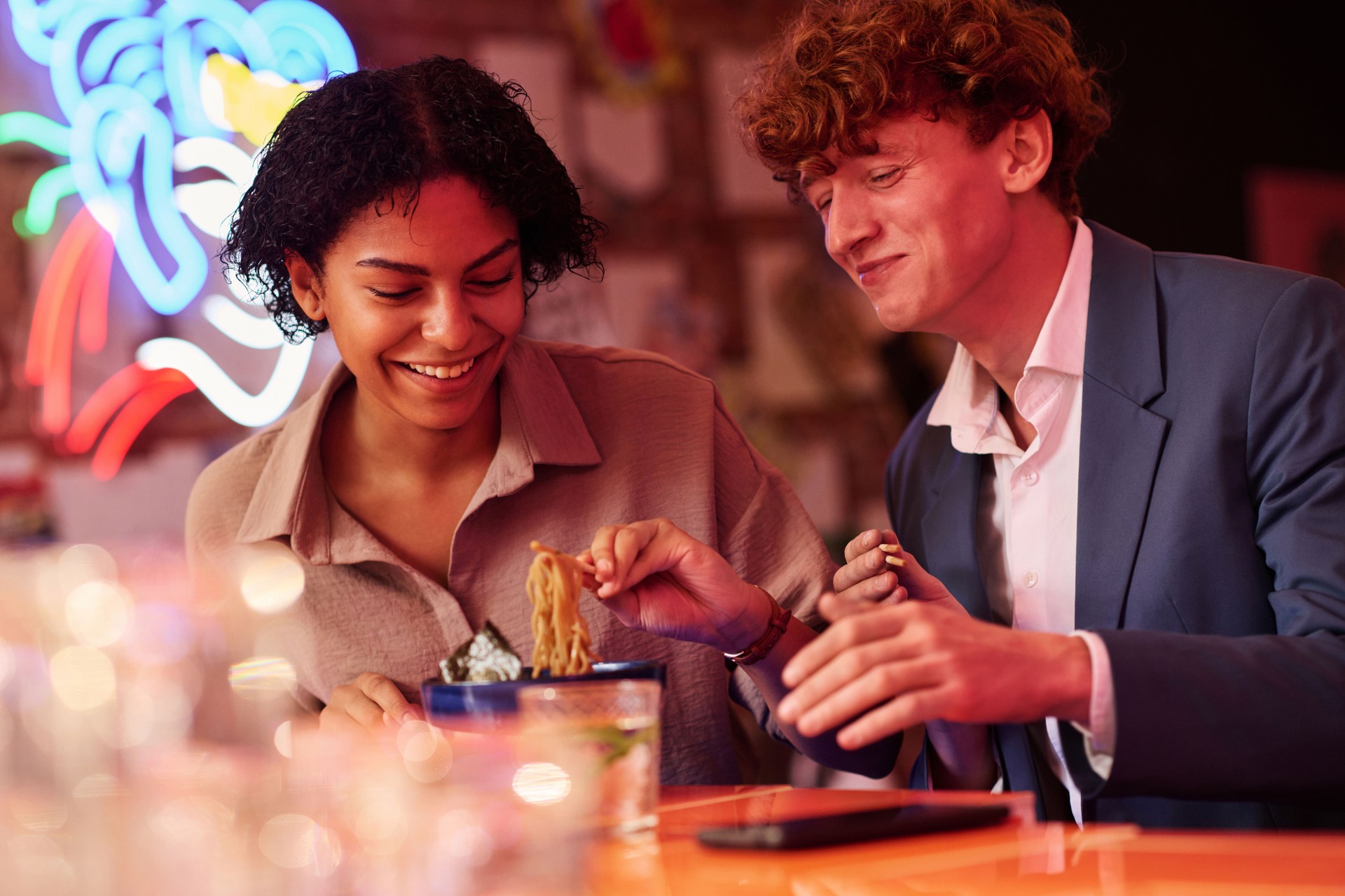Happy young dates or colleagues sitting by table in Japanese cafe or bar