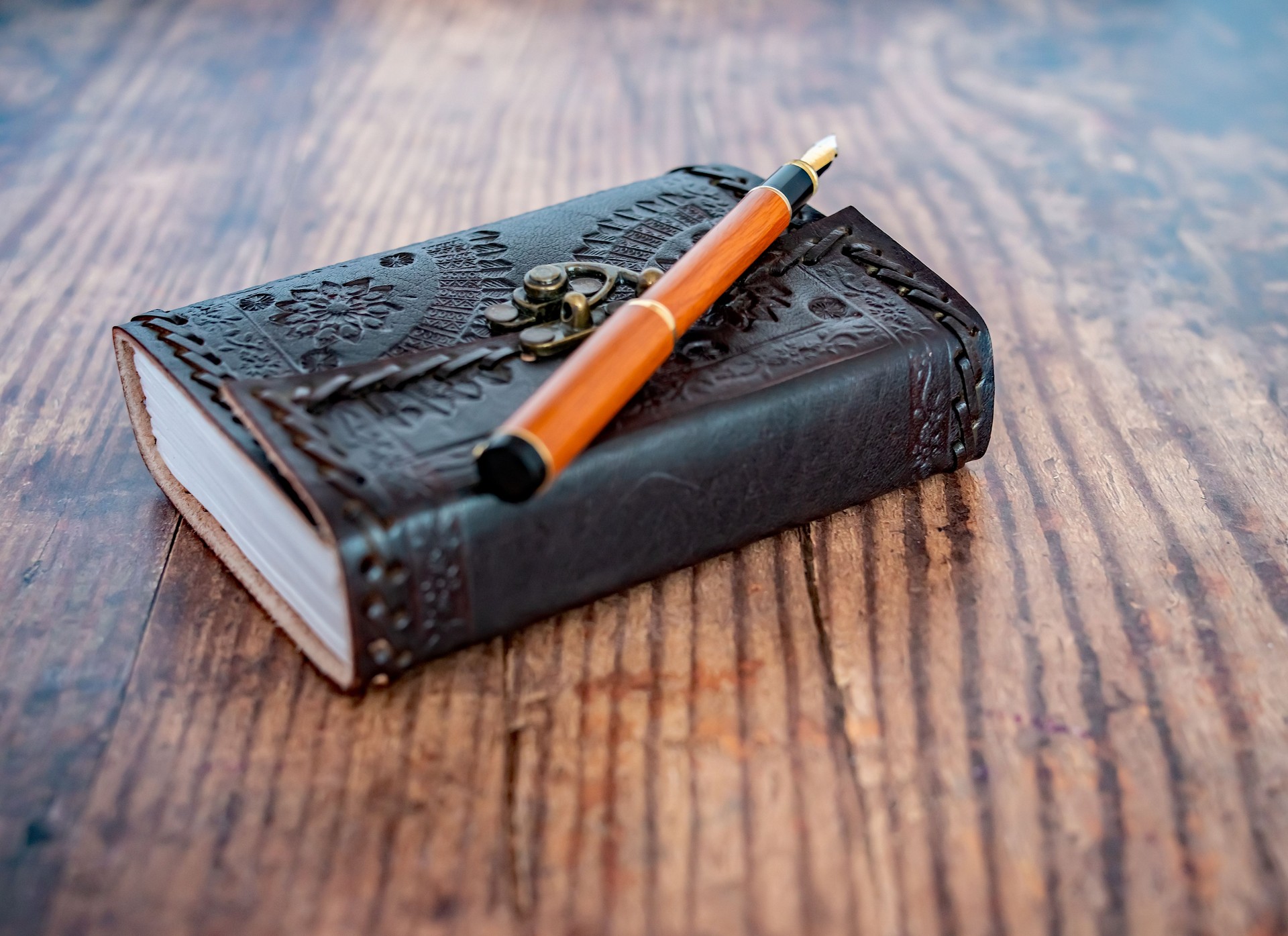 Side on view of leather bound notebook and wooden fountain pen on a wooden table